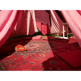 Das Bild zeigt einen roten Musterteppich, und rote Kissen unter Zeltwänden aus einzelnen roten Stoffbahnen.