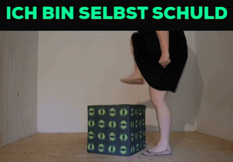 Ein Gif. Oben in Knallgrün auf Schwarzem Grund die Worte: ich bin selbst schuld. Darunter versucht Tristan Marie sich auf einen würfelförmigen Polsterhocker zu stellen. Nin findet kein Gleichgewicht und fällt seitwärts vom Hocker.