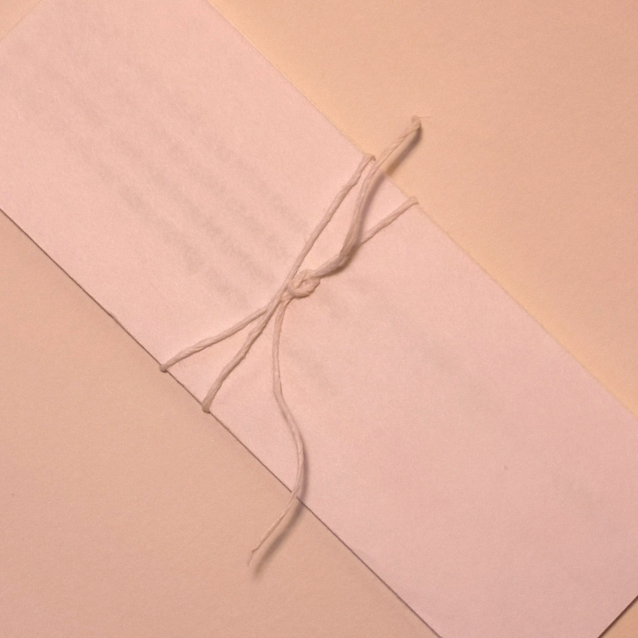 Ein Leporello aus weißem Papier. Das Leporello ist geschlossen. Um das Buch ist ein weißer Papierfaden gewickelt. Schrift scheint sanft durch das Papier durch.